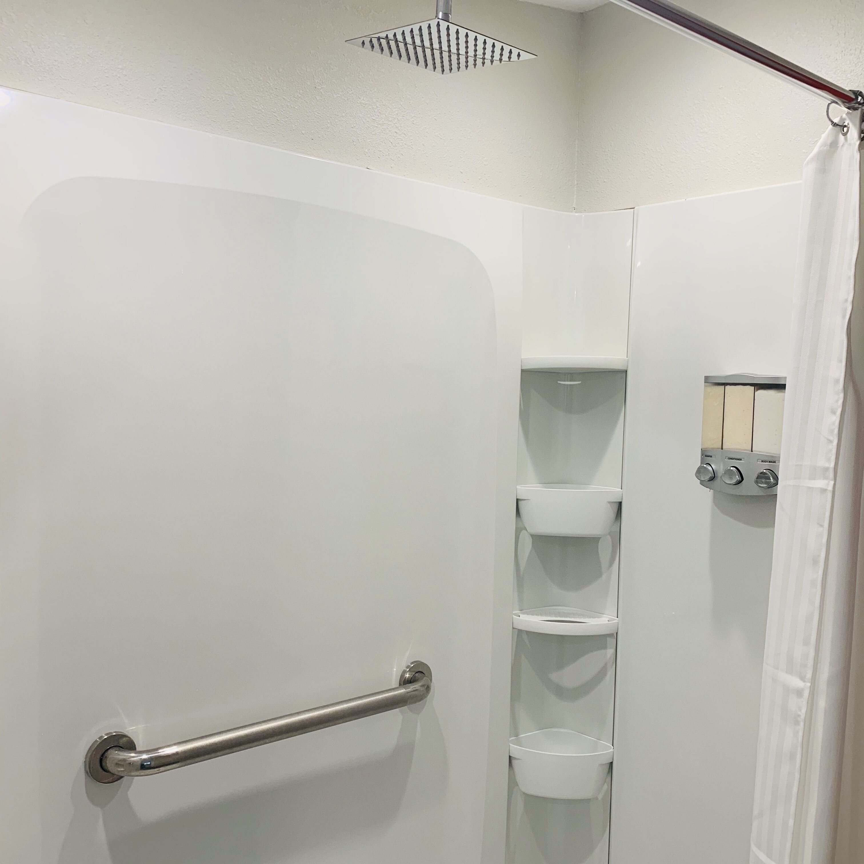 A white shower stall with a grab bar, a showerhead, and a control panel for water temperature and flow.