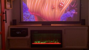 A television mounted on a wooden cabinet with a lower shelf displaying a decorative item. - Luxury Cottage in the Woods with Movie Theater!  (Auburn)