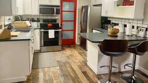 A modern kitchen with white cabinets, stainless steel appliances, a red-framed door, and a bar area with stools. - Luxury Cottage in the Woods with Movie Theater!  (Auburn)