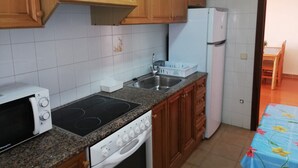 Eine Küche mit Holzausstattung, einer Mikrowelle, einem Induktionskochfeld, einem Spülbecken und einem Kühlschrank.