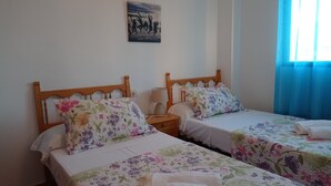 A hotel room with two single beds, floral bedding, a bedside table with a lamp, and a painting on the wall. - La Marina I 4º Solo Familias! (Xeraco Playa)