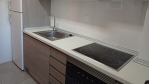 A modern kitchen with white cabinets, a stainless steel sink, a built-in stove, and a white refrigerator. - La Marina I 4º Solo Familias! (Xeraco Playa)