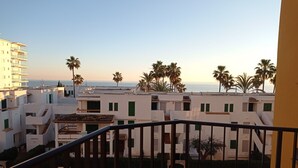 A balcony with a view of a coastal area, featuring white buildings, palm trees, and a clear sky. - La Marina I 4º Solo Familias! (Xeraco Playa)