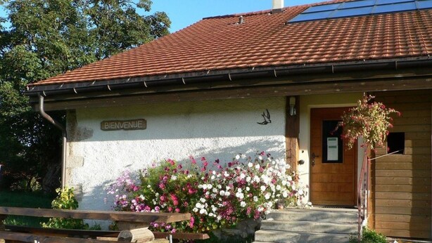 Un edificio con un cartel que dice 'BIENVENUE', un banco de madera y una cama de flores al frente.