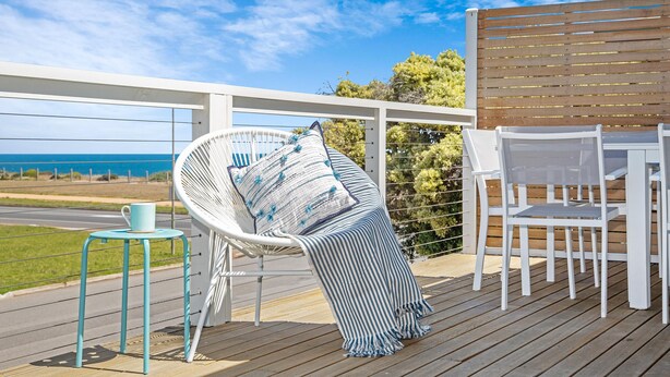 Una terraza con una silla blanca, una silla de mimbre y una mesa con una taza blanca.
