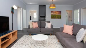 Una sala de estar moderna con un sofá gris, una mesa de centro blanca y un televisor sobre un mueble de madera.