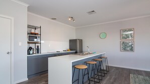Una cocina moderna con una isla central, taburetes de bar, un microondas y un refrigerador.