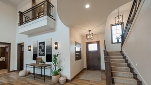 Un hallo espacioso con piso de madera, una escalera con peldaños alfombrados, una mesa con planta y un accesorio de iluminación instalado en la pared.