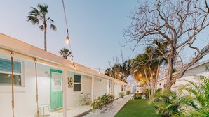 A row of white buildings with green doors, a grassy area, and palm trees.