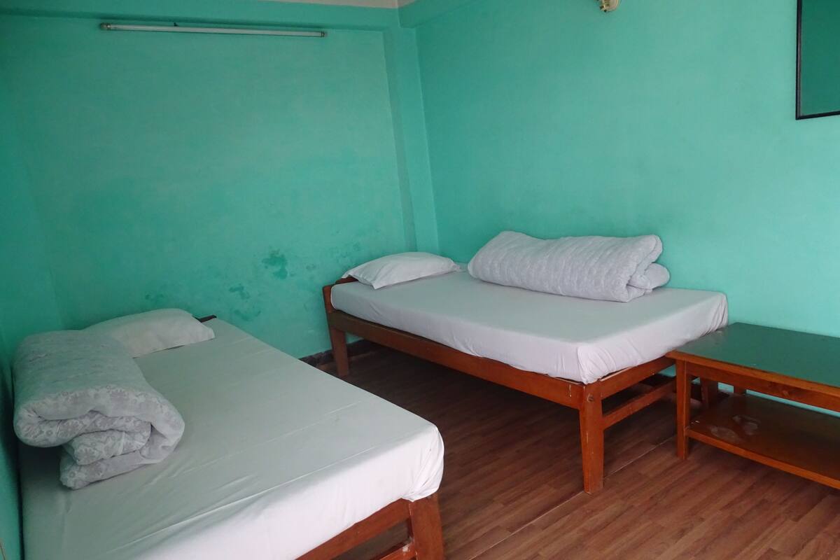 A room with two single beds, wooden flooring, and teal walls.