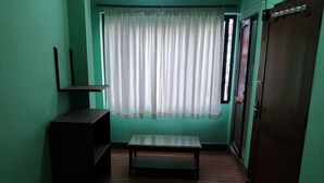 A room with a wooden bench, a dark-colored cabinet, a window with sheer curtains, and a door with a metal handle. - Green House Lodge (Kathmandu)