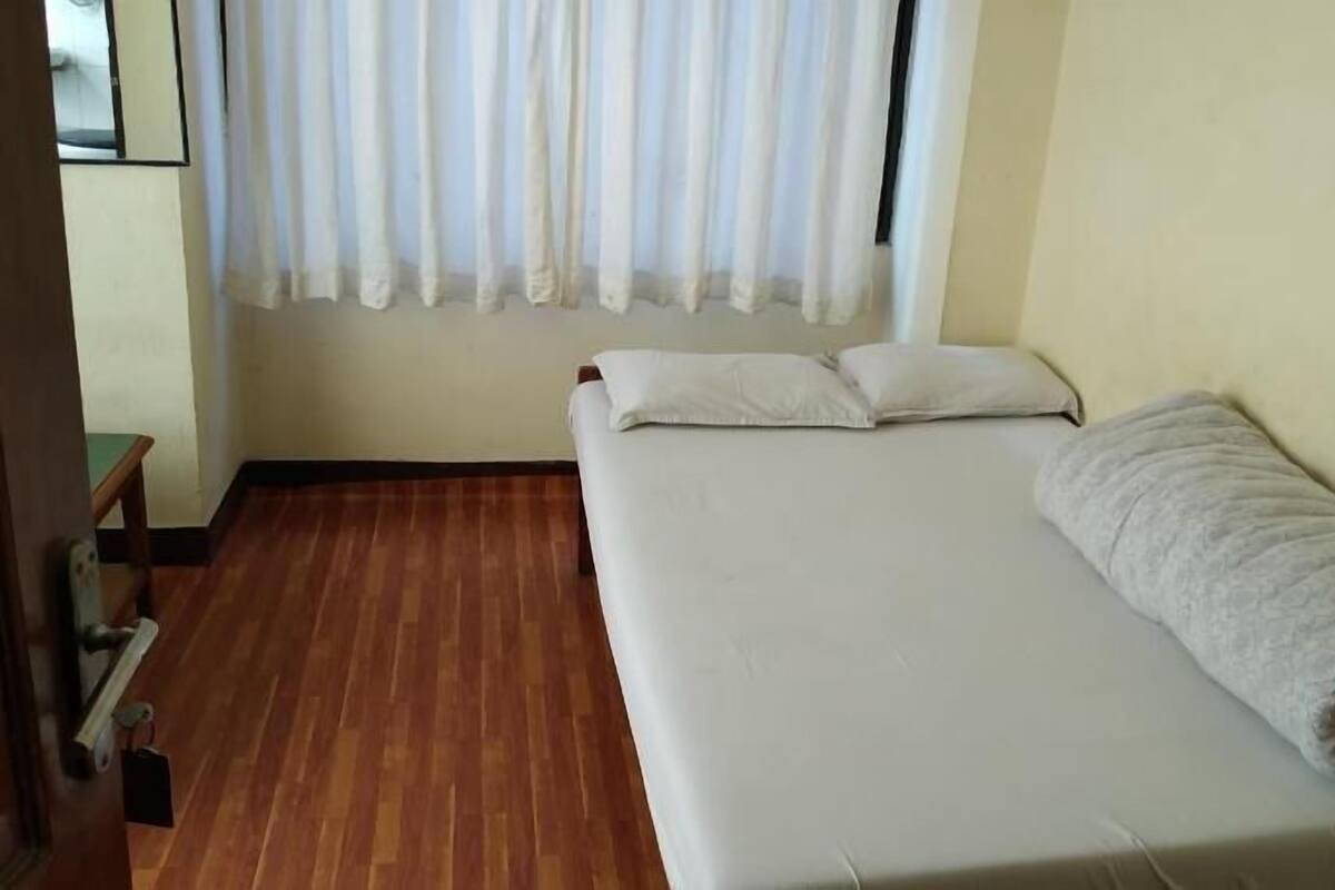 A single bed with white bedding and pillows, a rolled-up towel, and a wooden floor.