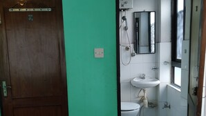 A bathroom with a wooden door, a sink, a toilet, and a shower. - Green House Lodge (Kathmandu)
