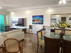 Uma sala de estar moderna com sofá, mesa de jantar, cadeiras, televisão e obras de arte.