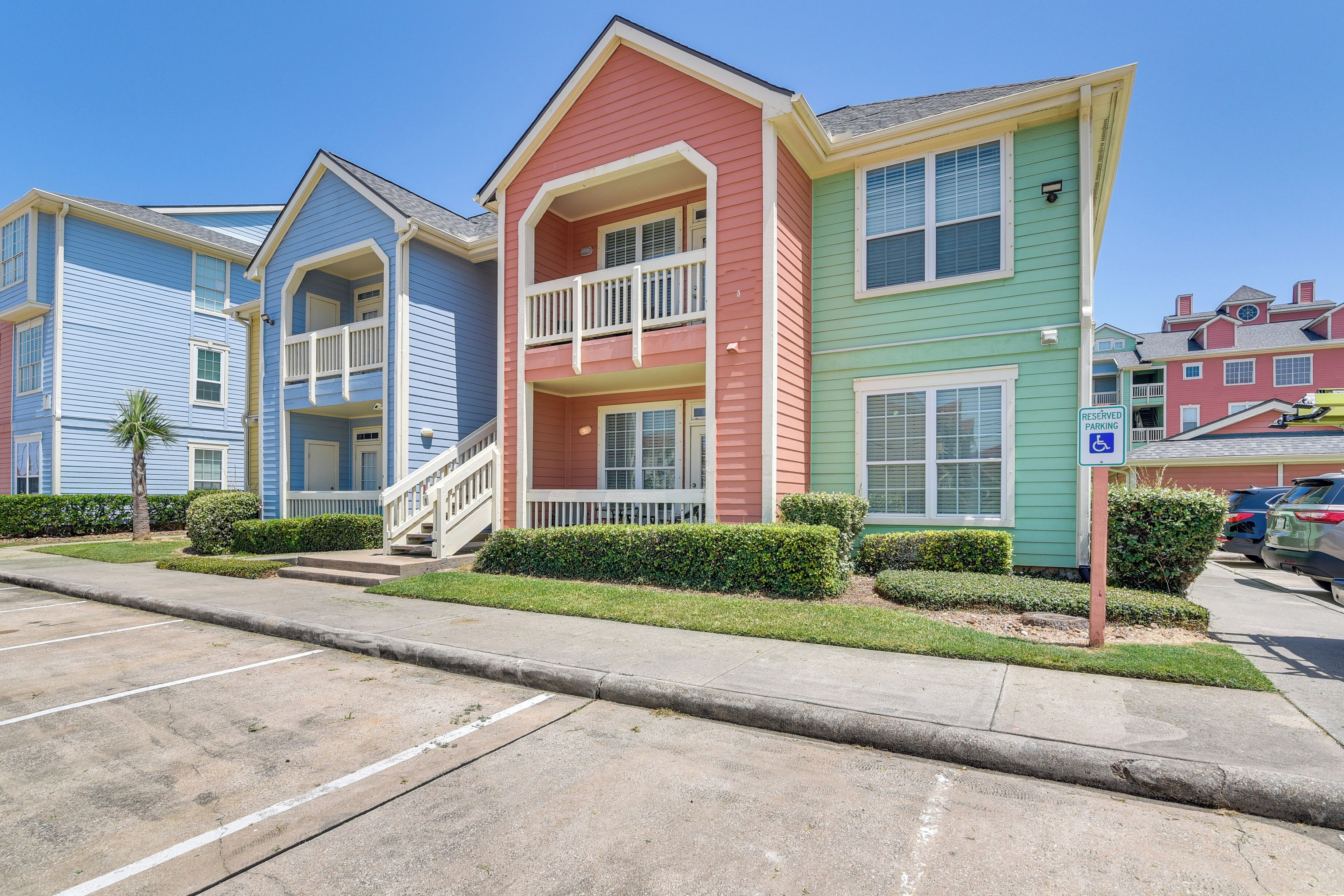 A row of colorful townhouses with a parking lot in front.