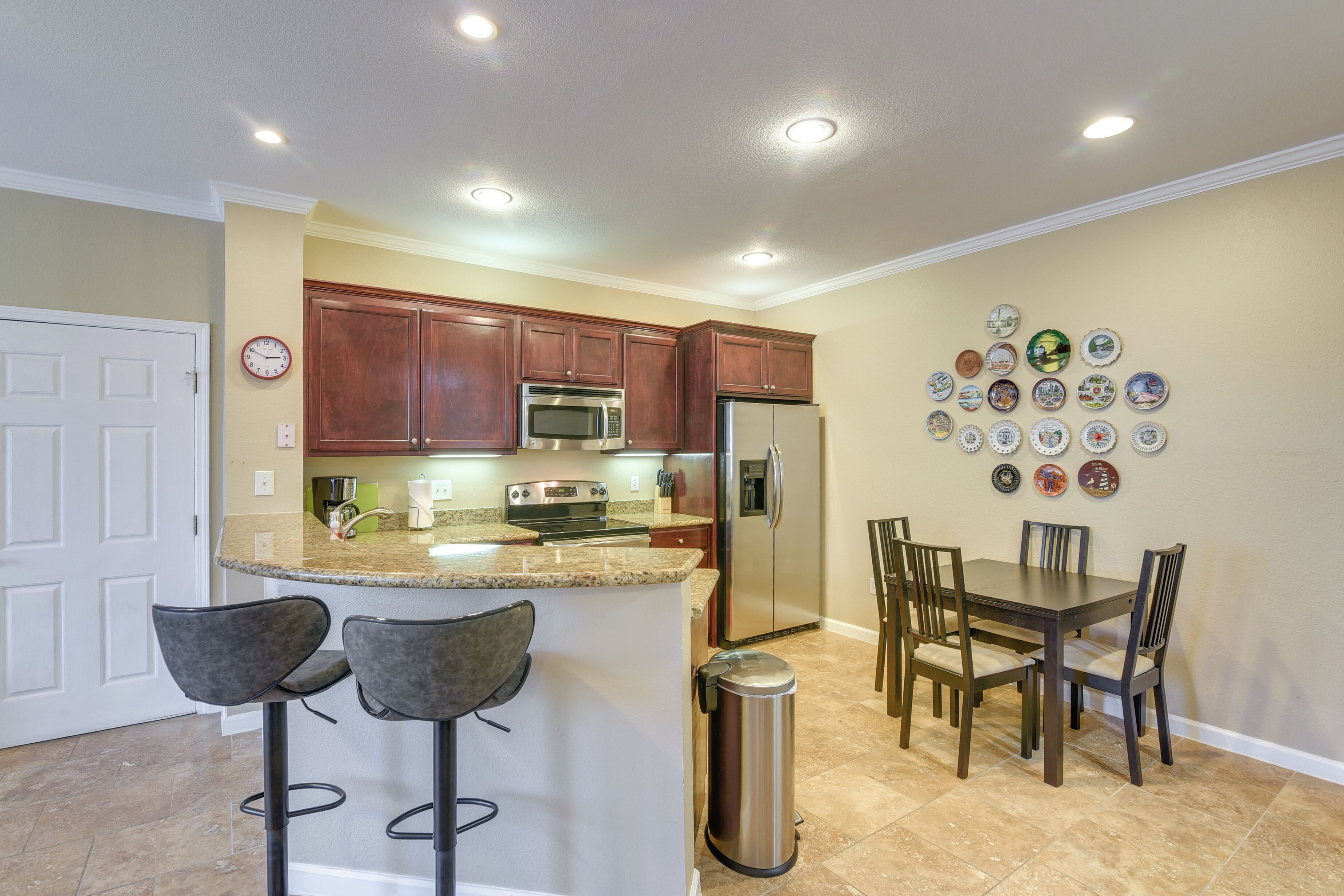 A kitchen with a central island, bar stools, a dining table with chairs, and a trash can.