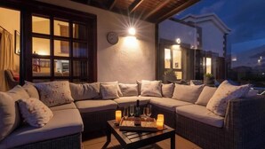 Un rincón exterior acogedor con sofá, cojines y una mesa con velas y copas.