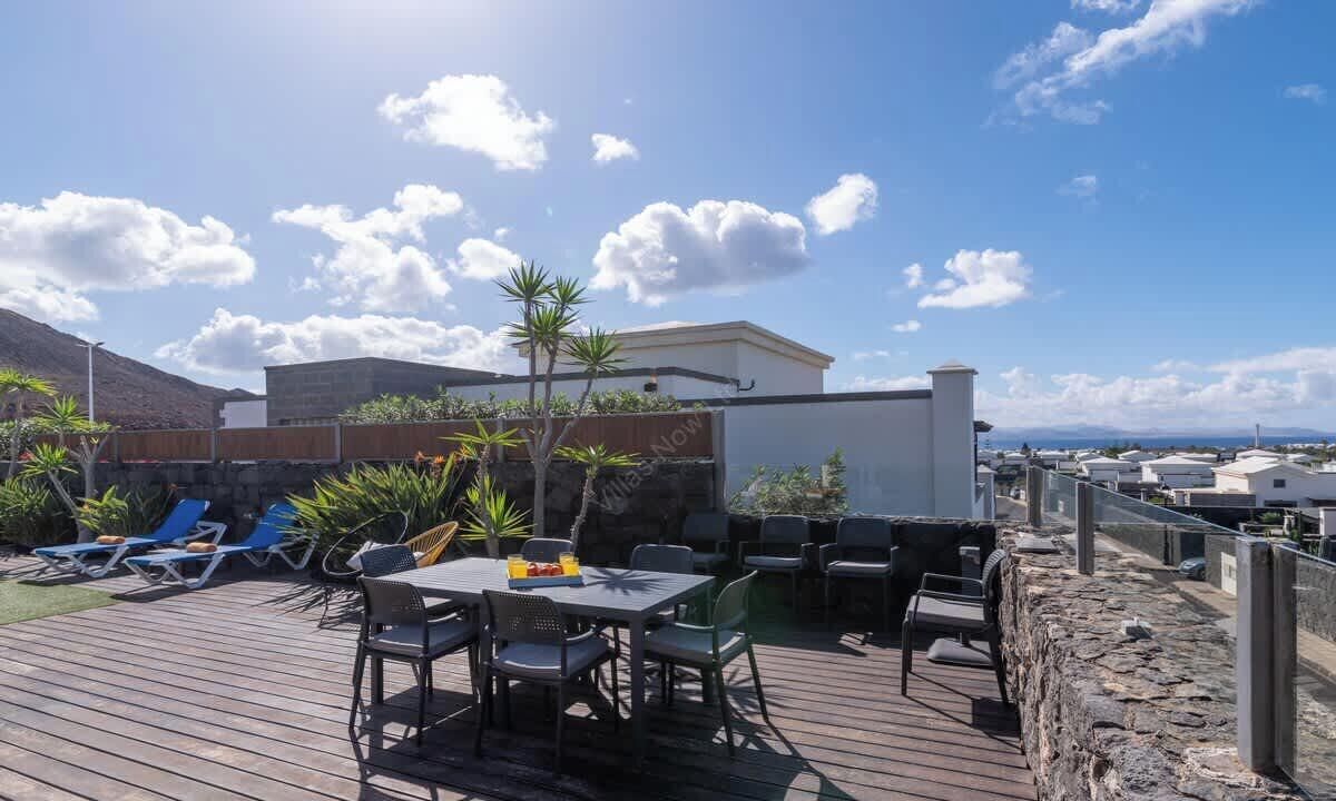 Een terras met tuinmeubilair, een tafel en stoelen, omgeven door planten en uitzicht op zee.