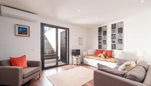 A modern living room with a sofa, a coffee table, a TV, and a staircase leading to an upper floor.
