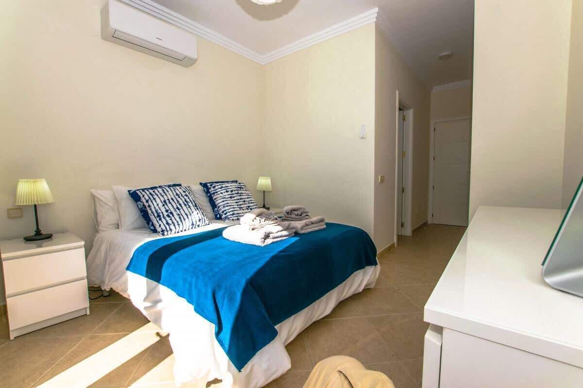 A bedroom with a bed, bedside tables, a desk, and an air conditioning unit.
