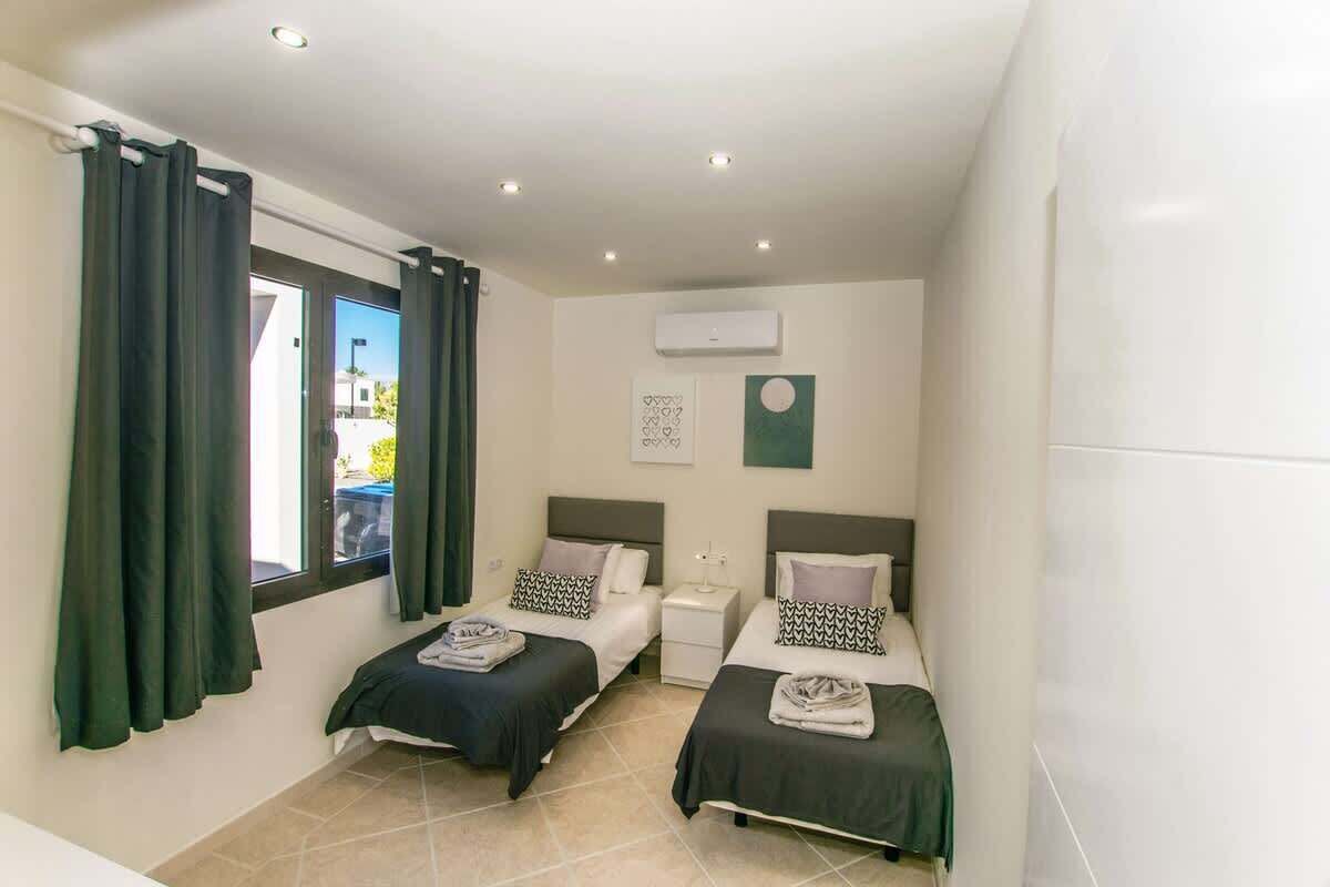 Un dormitorio con dos camas, una ventana con cortinas, un equipo de aire acondicionado y una obra de arte colgada en la pared.