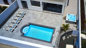 Un área de piscina en la azotea con sillones de descanso, un jacuzzi y una zona de estar cubierta.