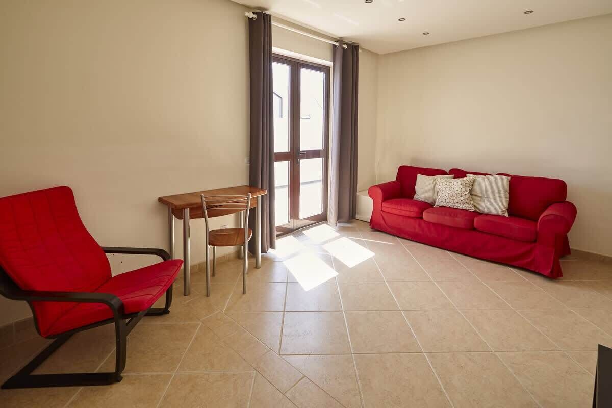 A living room with a red sofa, a red chair, a wooden table, and a large window with curtains.