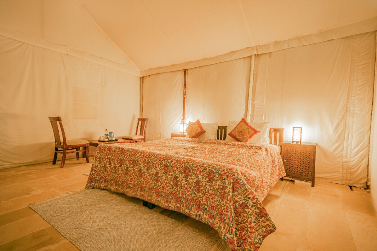 Una amplia habitación con tienda de campaña, una cama grande, dos sillas, una mesita pequeña y una mesita de noche.