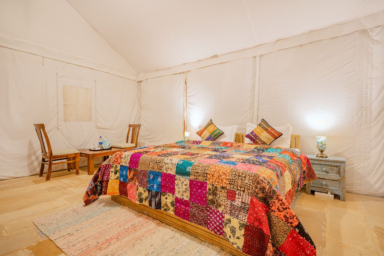 A tented room with a large bed, a chair, a small table, and a nightstand.