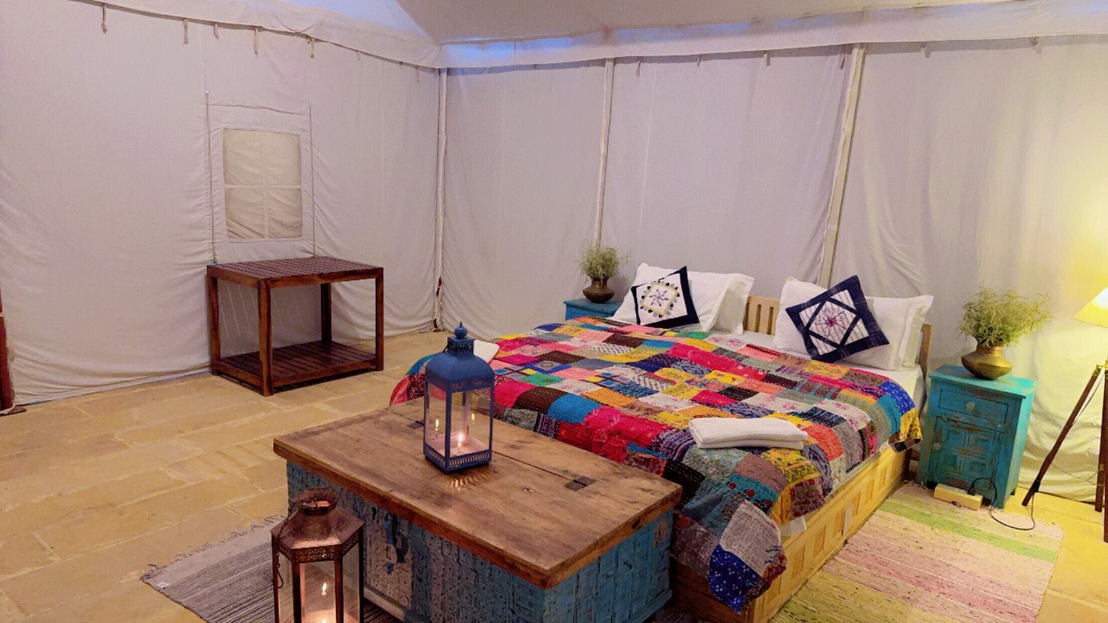 Une pièce aménagée avec une tente, un lit, une petite table, une lanterne et une table de chevet.