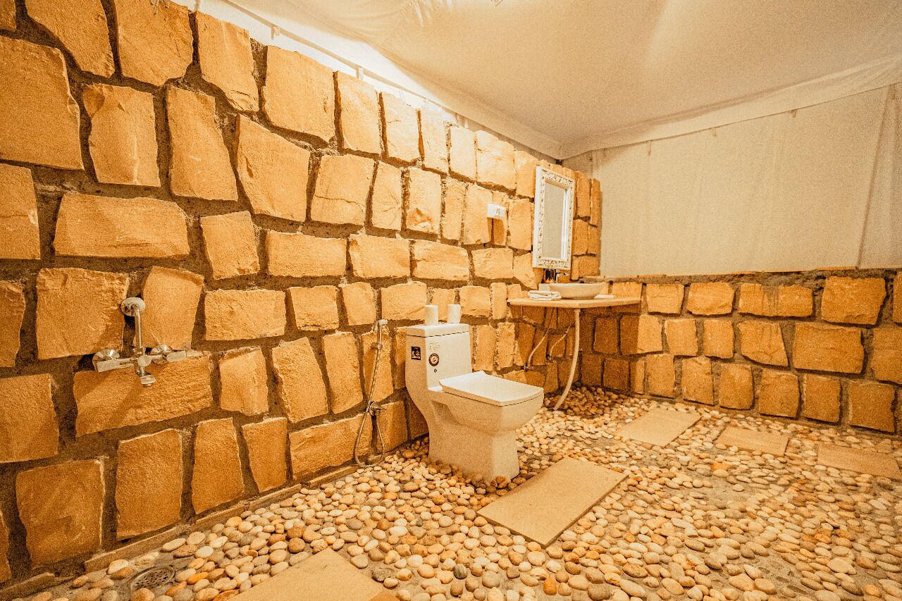Une salle de bain aux murs en pierre, équipée de toilettes, d’un lavabo et dotée d’un sol en pierre.