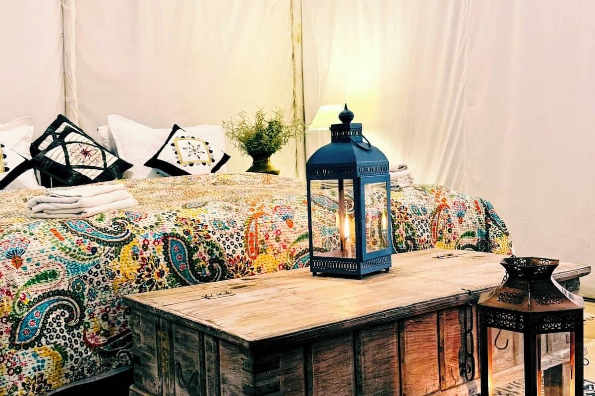 Una habitación con carpa, una cama, un banco y dos faroles.