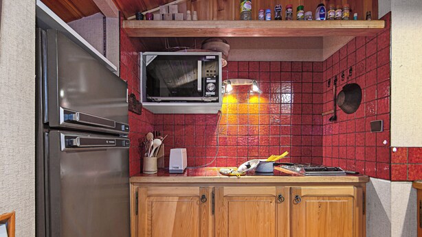 A kitchen with a stainless steel refrigerator, a microwave, wooden cabinets, and a red tiled backsplash. - La Persévérance15 - 2BR Sleeps 6 | Near Ski Lift & Mont Blanc Views, Argentière (Chamonix), France (Argentière (Chamonix))
