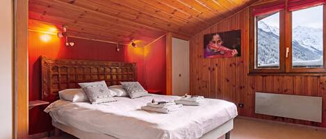 Ein Schlafzimmer mit Holzboden, einem Bett mit weißen Leinen, einem Nachttisch, einem Wandheizkörper und einem Fenster mit Blick auf die Berge.