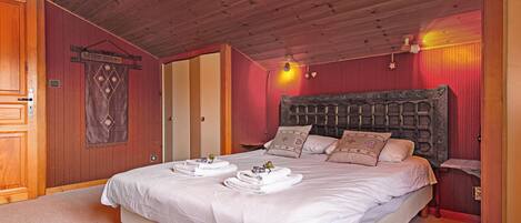 Une chambre d’hôtel avec un plafond en bois, un grand lit avec du linge de lit blanc et une tête de lit ornée d’un motif décoratif.