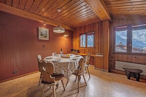 Ein Holzinterior mit einem Esszimmerstisch für vier Personen, einem Fenster mit Bergblick und einer Holzbalkendecke.