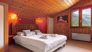 A bedroom with a wooden ceiling, a large bed with white linens, a painting on the wall, and a window with a mountain view. - La Persévérance15 - 2BR Sleeps 6 | Near Ski Lift & Mont Blanc Views, Argentière (Chamonix), France (Argentière (Chamonix))
