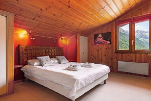 Ein Schlafzimmer mit Holzboden, einem großen Bett mit weißen Leinen, einem Gemälde an der Wand und einem Fenster mit Blick auf die Berge.