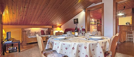 Un espace repas avec une table dressée pour quatre personnes, des chaises en bois et un haut plafond également en bois.