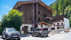 A multi-story building with a wooden facade, a balcony, and a parking area with two cars. - La Persévérance15 - 2BR Sleeps 6 | Near Ski Lift & Mont Blanc Views, Argentière (Chamonix), France (Argentière (Chamonix))