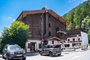 Ein mehrstöckiges Gebäude mit Holzfassade, einem Balkon und einem Parkplatz mit zwei Autos.