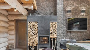A log cabin interior with a fireplace, stone wall, and a flat-screen TV mounted on the wall.