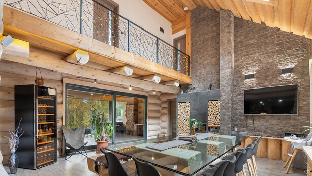 A spacious dining area with a glass table and black chairs, a wooden ceiling, and a stone wall.