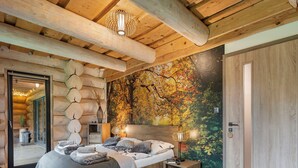 A log cabin bedroom with a large bed, wooden walls, a mural of autumn leaves, and a wooden door.