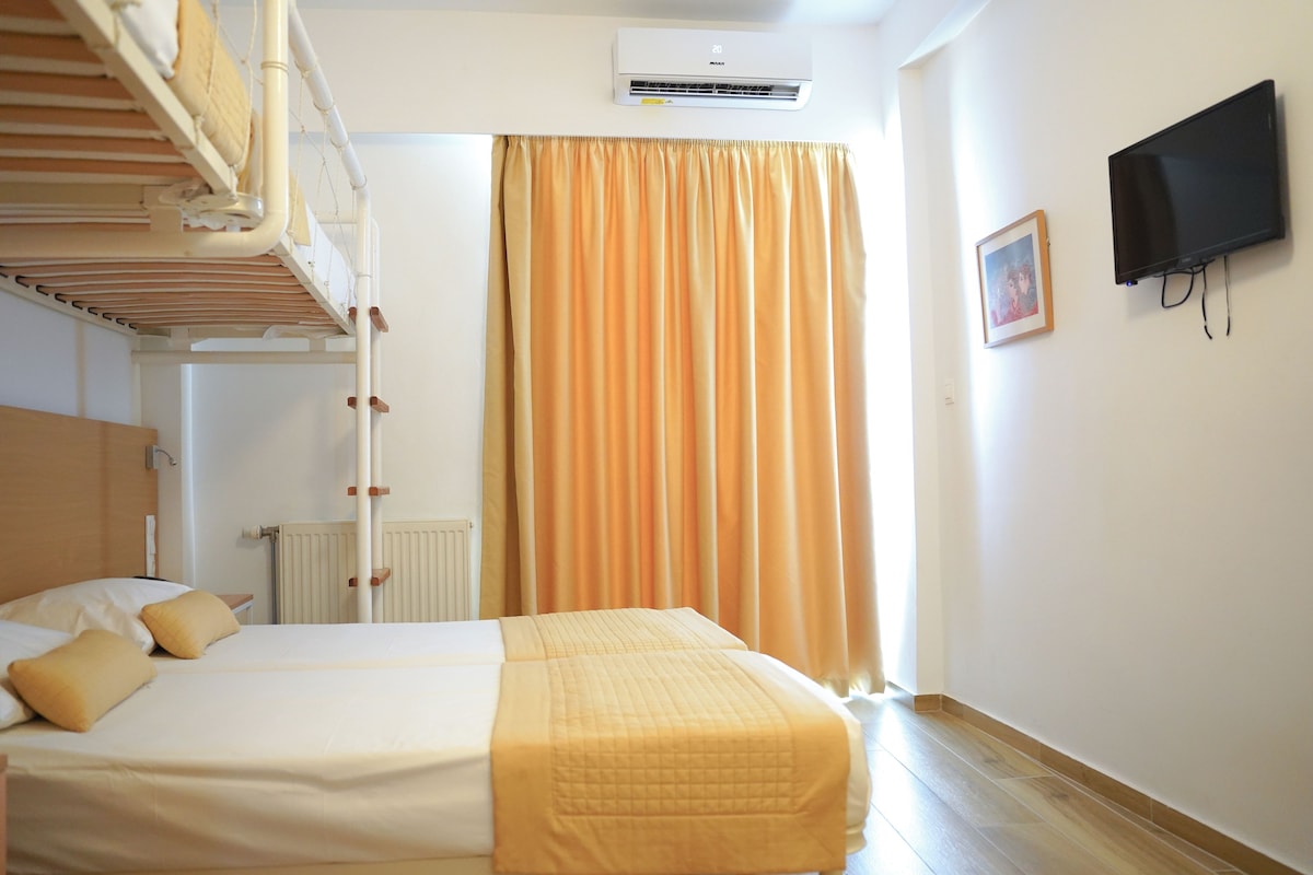 Una habitación de hotel con literas, una cama individual, un aire acondicionado, un televisor y un ventanal con cortinas.
