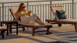 A person relaxing on a lounge chair by a pool with a view of the water and mountains in the background.