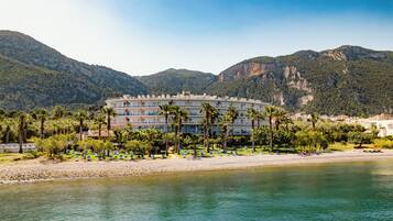 A hotel with a pool, surrounded by palm trees and mountains.