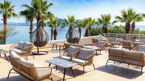 A terrace with wicker furniture, palm trees, and a view of the sea. - Sissy (Kamena Vourla)