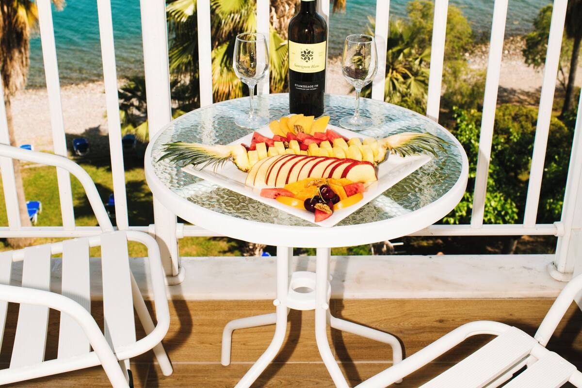 A balcony with a table set for a meal, overlooking a beach and ocean.