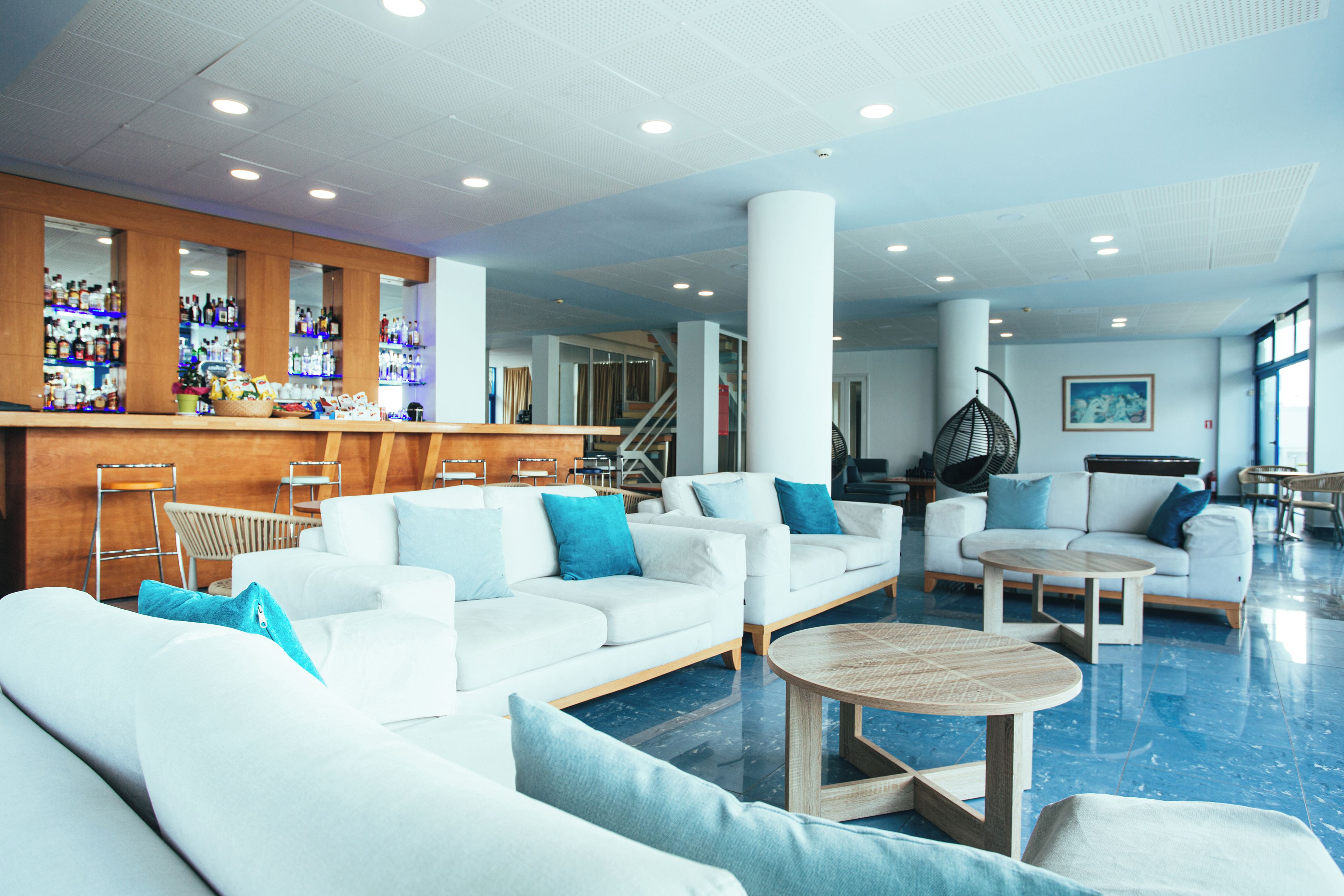 Um lobby de hotel moderno com sofás brancos, área de bar e uma escadaria.